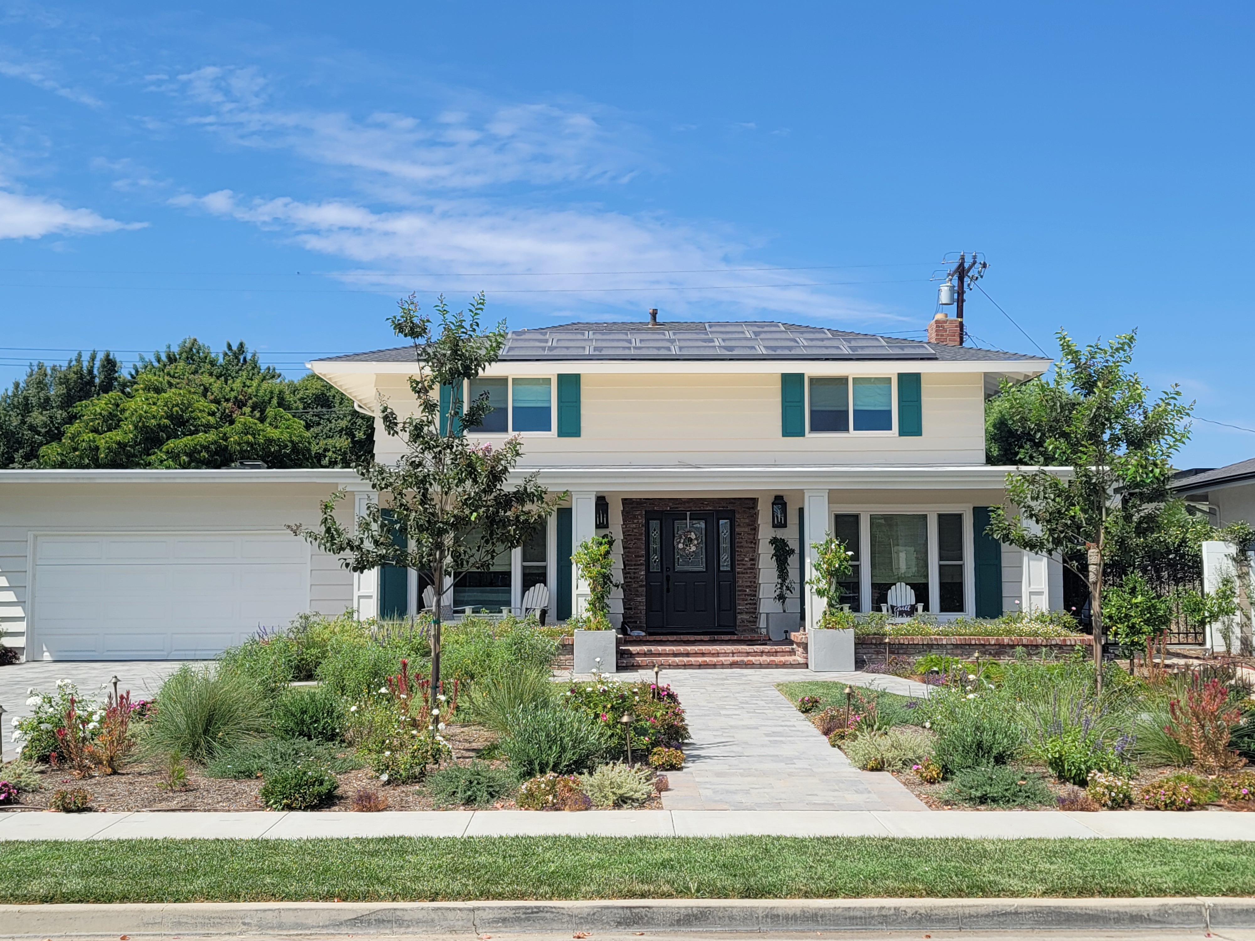 After view of the home exterior with white-framed windows, green shutters and a dark front door.