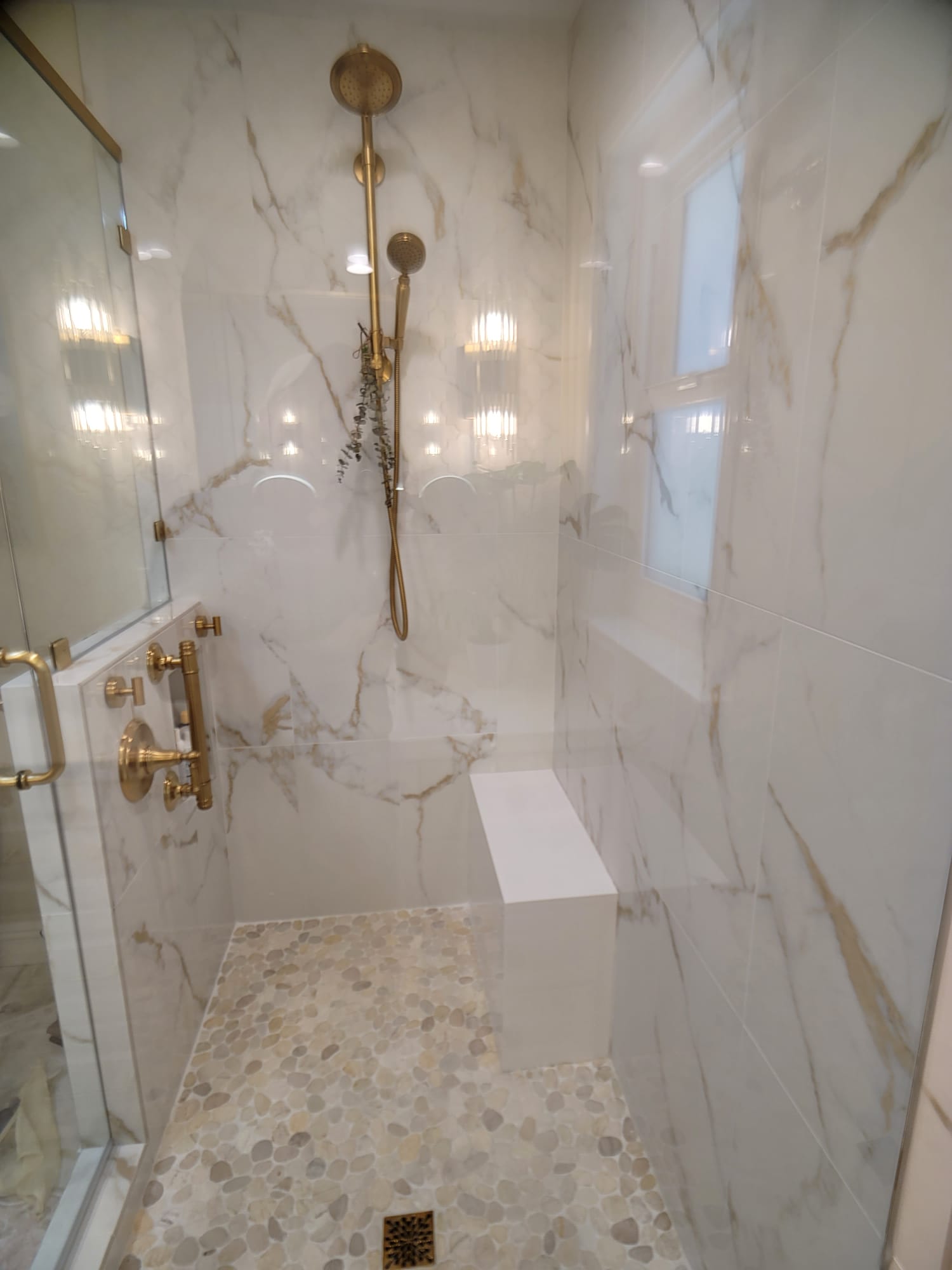 Walk-in shower interior with built-in bench, recessed niche, pebble floor, and brass rain shower Walk-in shower interior with built-in bench, recessed niche, pebble floor, and brass rain shower