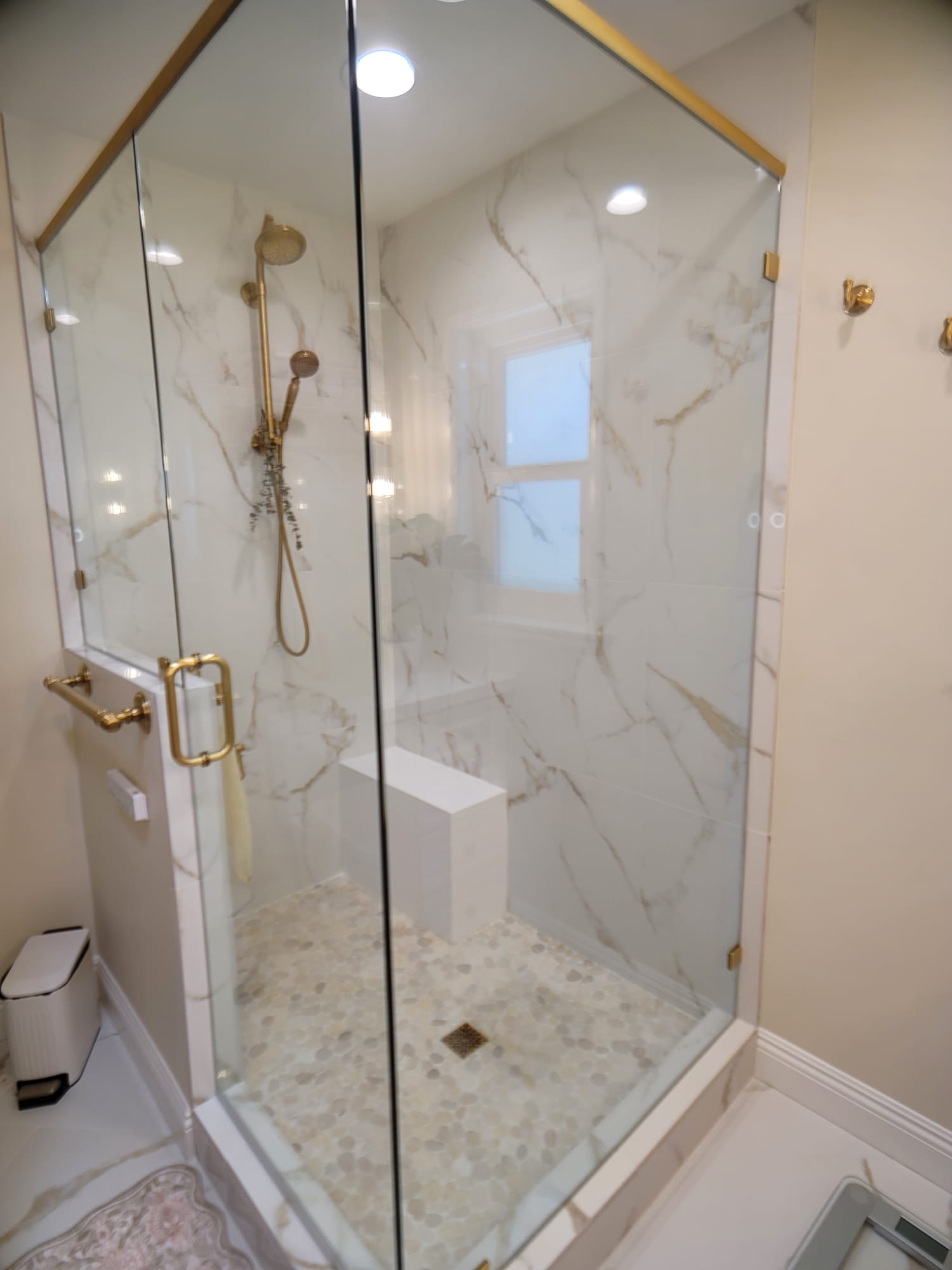 Frameless neo-angle glass walk-in shower with marble-look porcelain walls and brass hardware Frameless neo-angle glass walk-in shower with marble-look porcelain walls and brass hardware